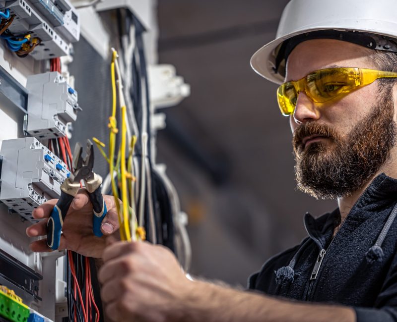 Male electrician at the checkout counter on a blurred background of a switchboard.